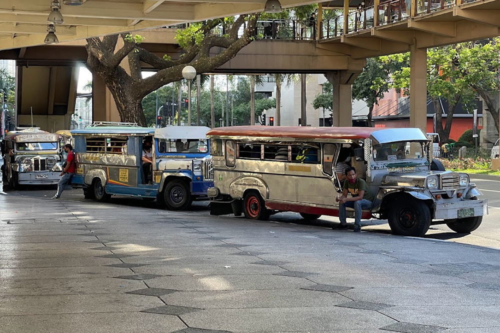 jeepneys lined up at a mall, with a barker sat by the first jeepney